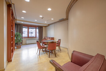 Main area of an office with a round meeting table with wooden furniture with a large wooden shelf for documents with air conditioning and heating and a large window with a view
