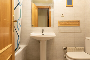 Bathroom with white porcelain sink on matching pedestal and frameless mirror attached to the wall