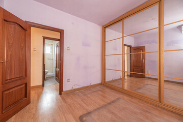 Empty bedroom with mirrored sliding door wardrobe and light oak parquet floor