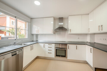 Fototapeta premium Large kitchen with bright white cabinets, stainless steel appliances and gray material countertop