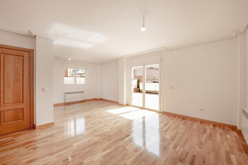Empty living room with glossy French oak parquet flooring and exit to a terrace with aluminum and glass doors