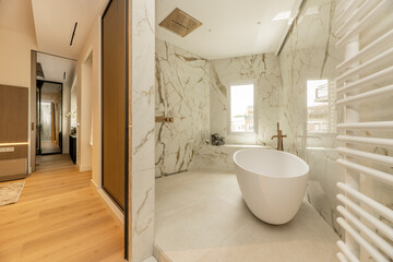 access from the bedroom to an en-suite bathroom with marble walls, continuous worktop in the same material, brass taps, rough marble floor and white freestanding bathtub