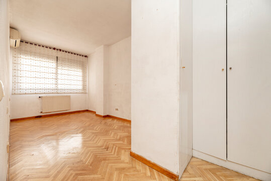 Empty bedroom with white wooden fitted wardrobes and herringbone oak parquet flooring