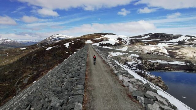 Aerial Follow Shot Behind Male Cycling Across Sysendammen In The Municipality Of Eidfjord in Hordaland, Norway