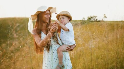 Mother carries child his arms. Family walk through hilly field and picking flowers
