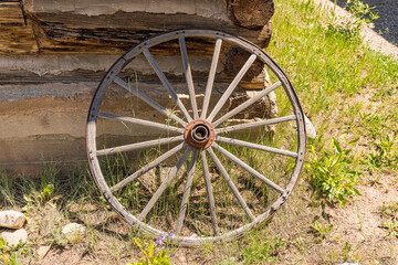 Fototapeta premium Old weathered wagon wheel leaning against a log cabin wall