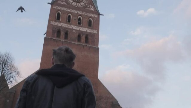Young Man in Leather Jacket walking to Church with Bird Flying Above