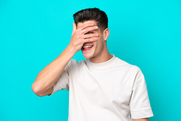 Young handsome caucasian man isolated on blue bakcground covering eyes by hands and smiling
