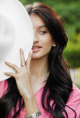 Portrait of a young girl standing in park, covering part of her face with a white hat.