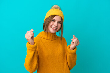 Young English woman wearing winter jacket isolated on blue background making money gesture