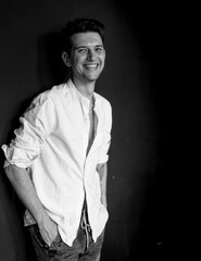 Studio shot of young handsome rebellious man in white shirt against black background in black and white. Monochrome portrait of young happy attracitive man.