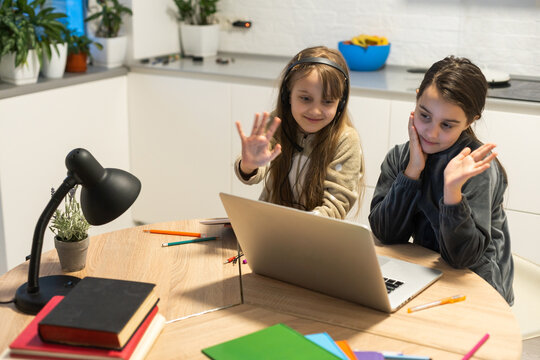 Two child girl students study online with teacher by video call together. Siblings are homeschooling with computer laptop during quarantine due to Covid 19 pandemic.