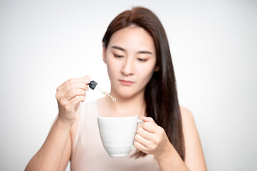 Woman dripping cbd oil inside tea cup, cofee cup - Alternative medicine, vitamins and supplements concept - Focus on dropper
