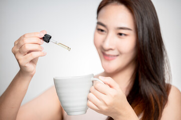 Woman dripping cbd oil inside tea cup, cofee cup - Alternative medicine, vitamins and supplements concept - Focus on dropper