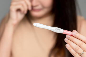 Asian woman holding pregnancy test feeling disappointed by negative result female health problems...
