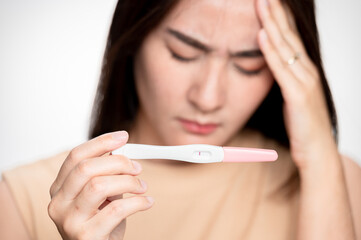 Asian woman holding pregnancy test feeling disappointed by negative result female health problems...