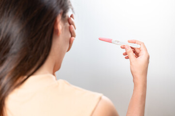 Asian woman holding pregnancy test feeling disappointed by negative result female health problems...