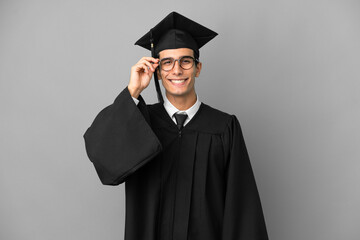 Young Argentinian university graduate isolated on grey background with glasses and happy