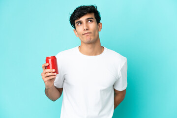Young Argentinian man holding a refreshment isolated on blue background and looking up