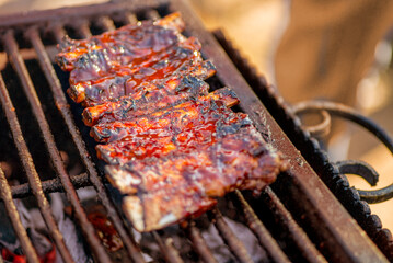 Barbecue ribs. Man in gloves flips grilled ribs on a charcoal grill. Picnic in the backyard during a family holiday. BBQ meat.