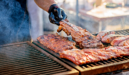 Barbecue ribs. Man in gloves flips grilled ribs on a charcoal grill. Picnic in the backyard during...