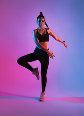 Athlete asian sportswoman jumping dance as part of fat burning workout in fitness studio neon background. Woman exercising with cardio at the gym.