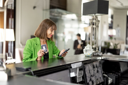 Young stylish business woman stands with phone on reception of luxury hotel. Woman check in hotel during a business trip