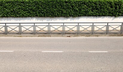 Protection railing on the roadside. Sidewalk and house fence, consisting of a white  wall and a...