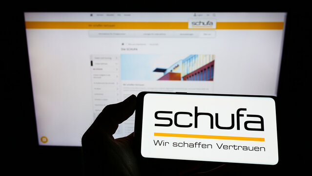 Stuttgart, Germany - 02-13-2022: Person holding smartphone with logo of German credit protection company Schufa Holding AG on screen in front of website. Focus on phone display.