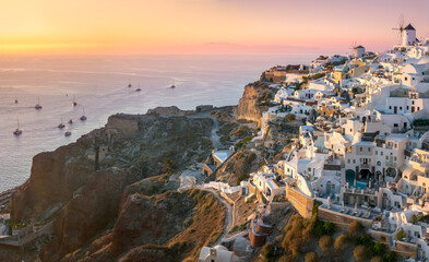 Santorini at Sundown. The famous town of Oia in the sunset. A line of sailing yachts at sea....