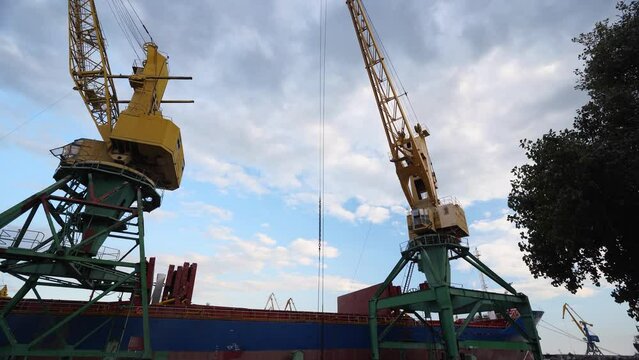 Grain transshipment from container to ship cargo holds with a dual scoop clamshell grab on crane in sea port. Wheat shipment with water transport. Agricultural commodities transportation. Timelapse.