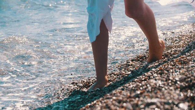 A woman walks on the pebbles and wetting her feet in sea water