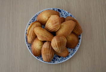 French madeleine cakes on a white and blue plate against a wooden table. 