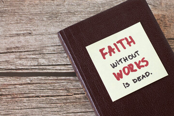 Obraz premium Faith without works is dead, a handwritten quote on a note on top of a closed Christian Holy Bible Book placed on a wooden table. Copy space. Trust and obedience concept. James 2:26 verse. Top view.
