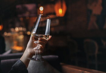 Female hand with french manicure holding a glass with wine on naturally blurred background. Woman in restaraunt. Luxury pasttime, celebration concept. 