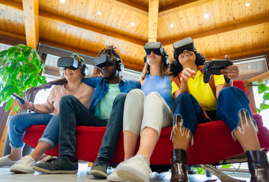 Group of international friends wearing a new futuristic virtual technology with headsets while sitting on couch - Team of creative friends working a futuristic project with goggles in AR.