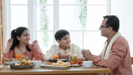 Happy Indian family enjoy eating food with hands, South Asian father and children wear traditional...