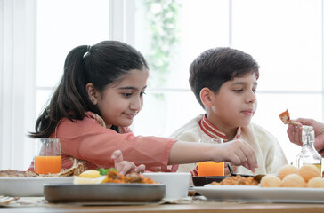 Happy Indian family enjoy eating food with hands, selective focus on South Asian cute girl holding...