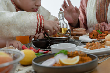 Selective focus on Indian boy hand holding naan bread dipping curry in dish enjoy eating food with hands, wearing traditional clothes, sitting with family at dining table. Indian culture lifestyle