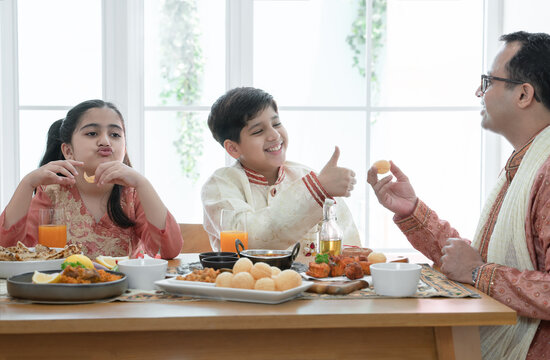 Happy Indian Family Enjoy Eating Food With Hands, South Asian Father And Children Wear Traditional Clothes, Sitting At Dining Table At Home Together. Indian Culture Lifestyle.