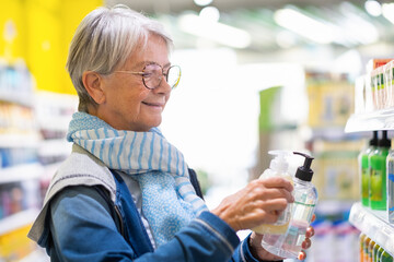 Fototapeta Portrait of caucasian elderly woman making purchase in supermarket, elderly smiling lady selecting and checking prices of hand liquid soap obraz