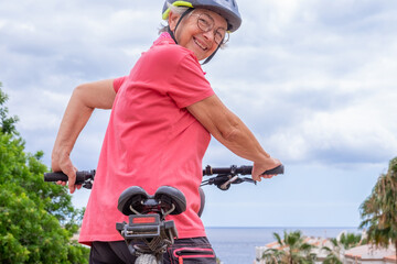 Rear view of smiling caucasian cyclist senior woman in pink t-shirt running along the sea in summer...