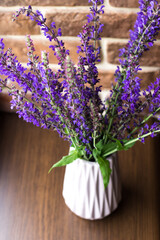 Flowering sage flowers. Bouquet of purple flowers by the window against the background of a brick wall