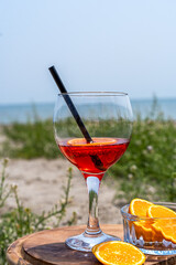 Cocktail glass of an Italian appetiser Gingerino drink, cut oranges on the beach with sea coast view