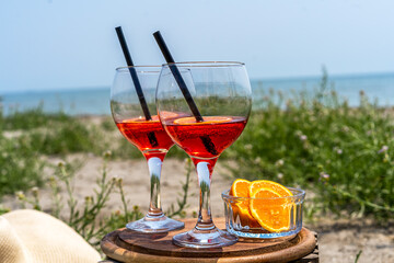 Two glasses of an Italian appetiser Gingerino drink, cut oranges on the beach with sea coast view