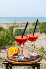 Two glasses of an Italian appetiser Gingerino drink, cut oranges on the beach with sea coast view