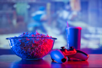 Cozy home relaxation near the TV - popcorn in a transparent glass bowl, soda drink in a plastic...