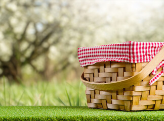 Picnic basket on green grass against the backdrop of beautiful nature. Spring, flowering trees, the beauty of nature. Rest, healthy lifestyle, romance. There is free space to insert.
