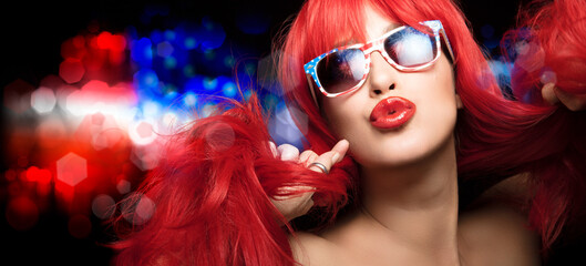 Sexy woman with red hair wearing American flag sunglasses, celebrates 4th July, pouting her...
