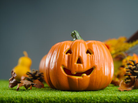 On the green grass, an orange pumpkin with a carved face, a smile, fruits, cones, autumn leaves on a gray background. Symbols of the autumn holiday - Halloween. There is free space to insert.
